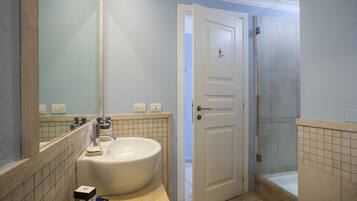 A bathroom with a large sink, a mirror, a door leading to another room, and a shower area.