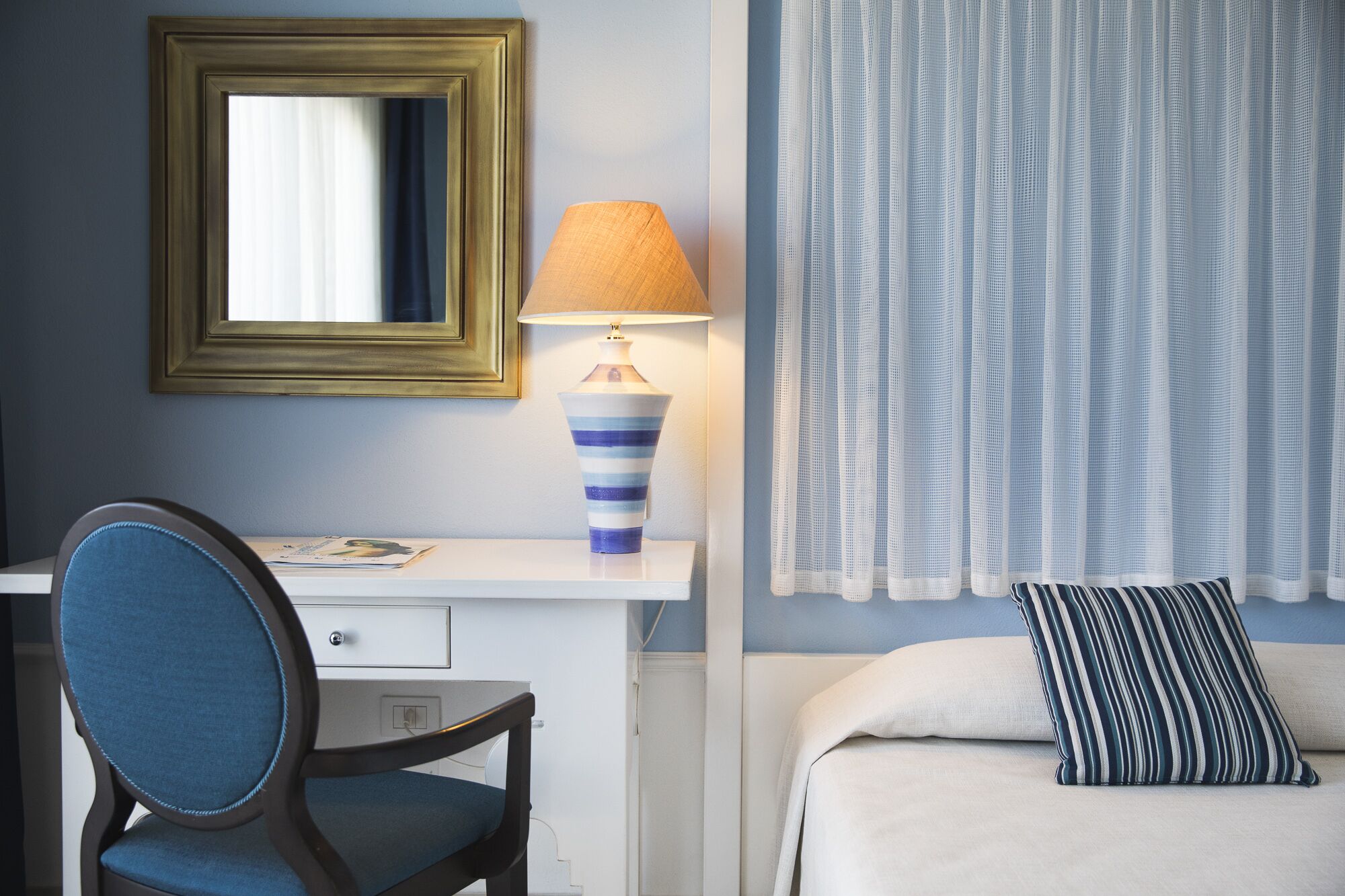 Ein Hotelzimmer mit Schreibtisch, Stuhl, Lampe, Bett und Vorhängen.