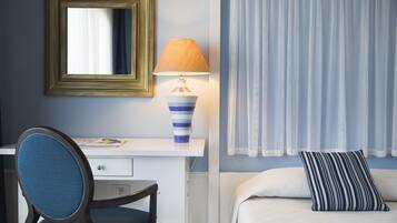 Ein Hotelzimmer mit Schreibtisch, Stuhl, Lampe, Bett und Vorhängen.