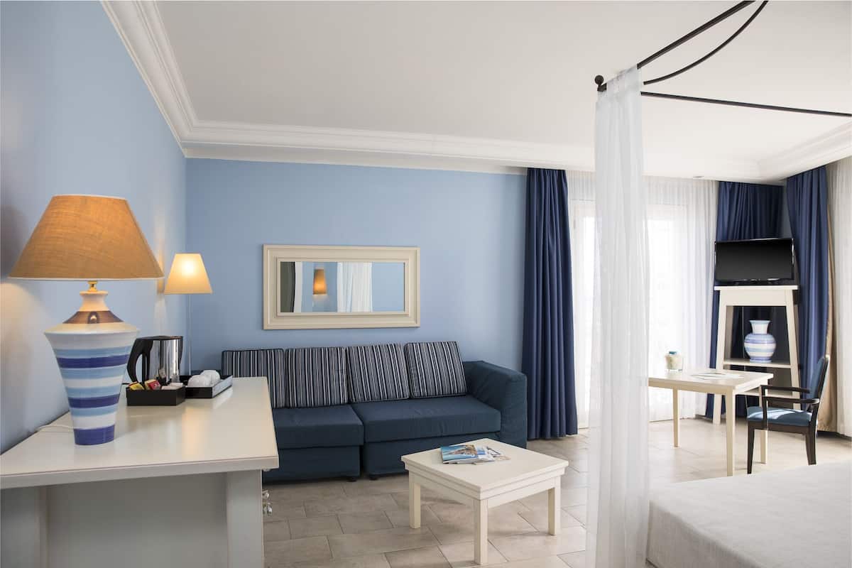 Ein Hotelzimmer mit einer Couch, einem kleinen Tisch, einer Lampe, einem Spiegel und einem Fernseher.