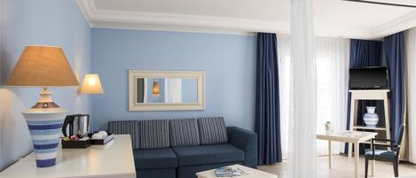 Habitación de hotel con sofá, una mesita, lámpara, espejo y televisor.
