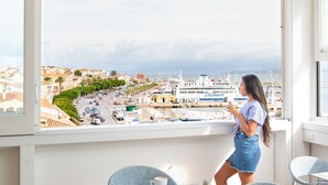 A balcony with a table set for breakfast, overlooking a marina with boats and a cityscape. - Lu' Hotel Carloforte (Carloforte)