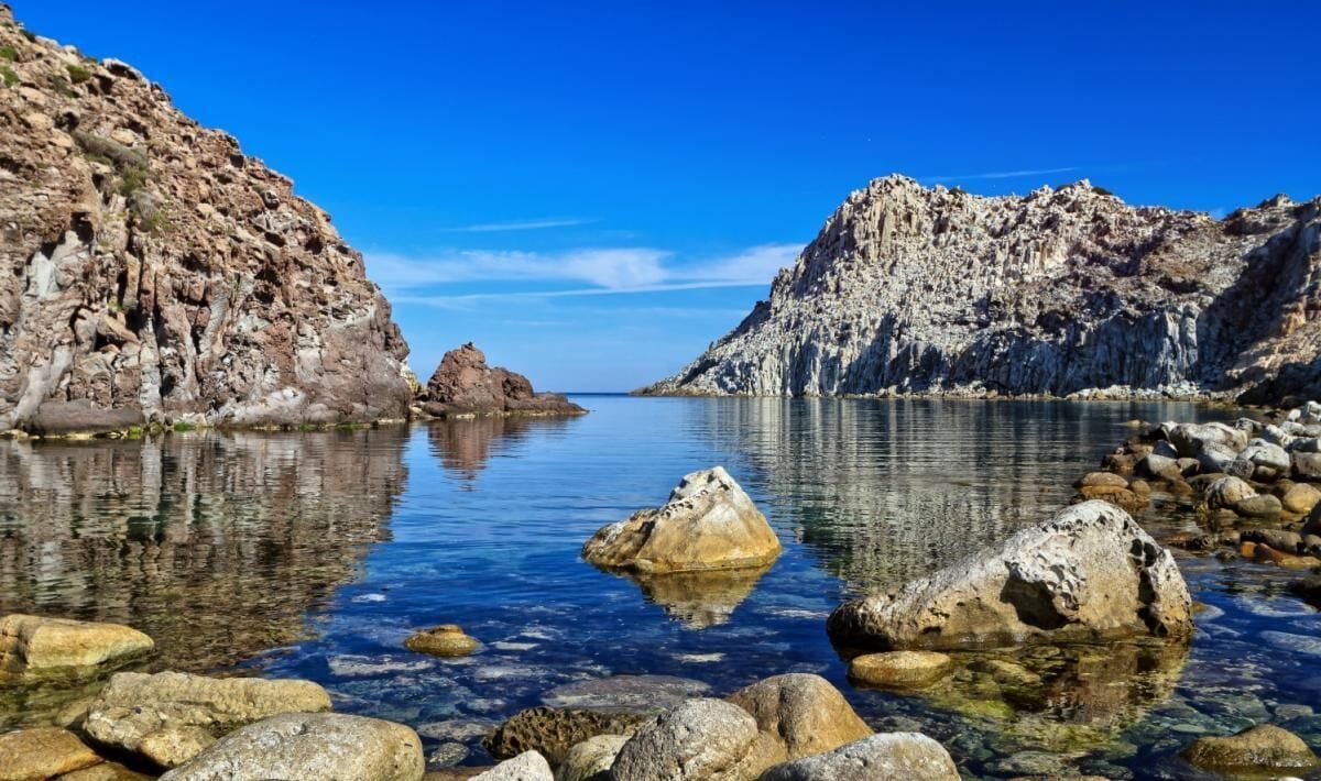 A rocky shoreline with clear water reflecting the surrounding cliffs.