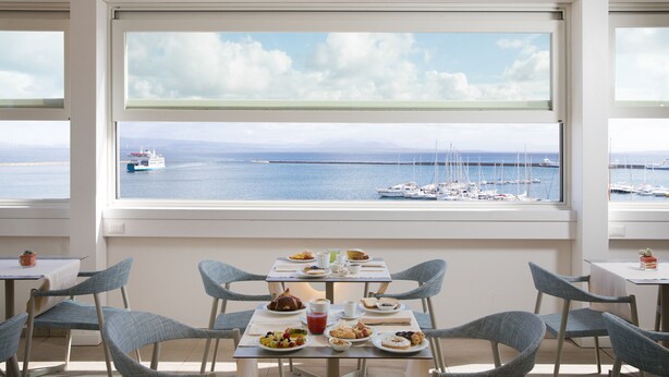 A dining area with a table set for two, overlooking a marina with boats and a clear sky.