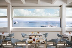 Un comedor con una mesa dispuesta para dos personas, con vistas a un puerto deportivo con barcos y cielo despejado.