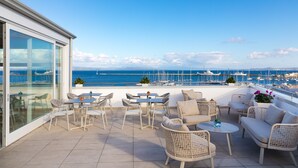 A terrace with outdoor furniture, a view of the sea, and a marina in the background. - Lu' Hotel Carloforte (Carloforte)