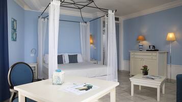 A bedroom with a four-poster bed, a bedside table with a lamp, a chair, and a small table with a vase and magazines.