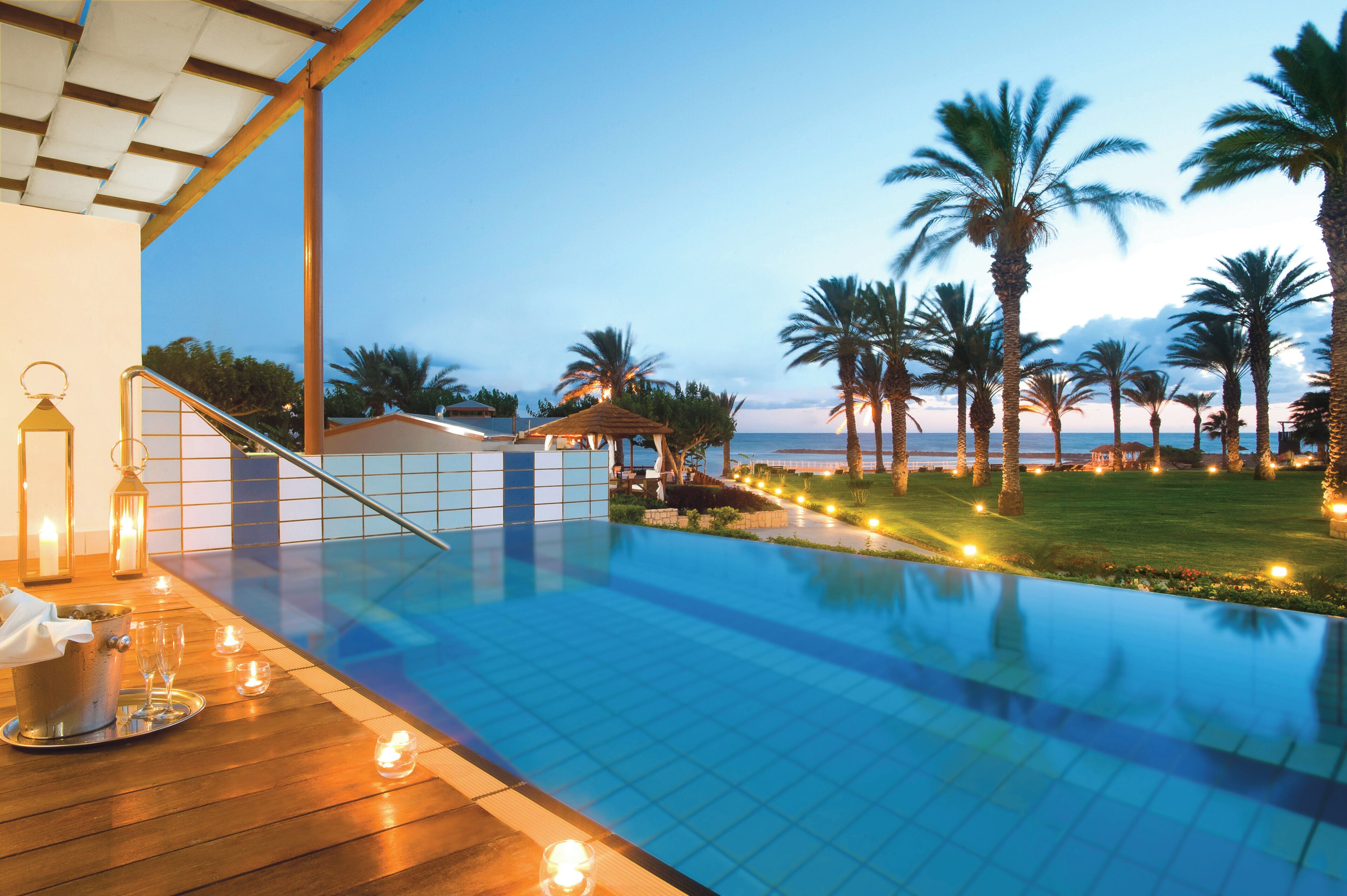 A poolside area with a view of the sea, palm trees, and a gazebo.