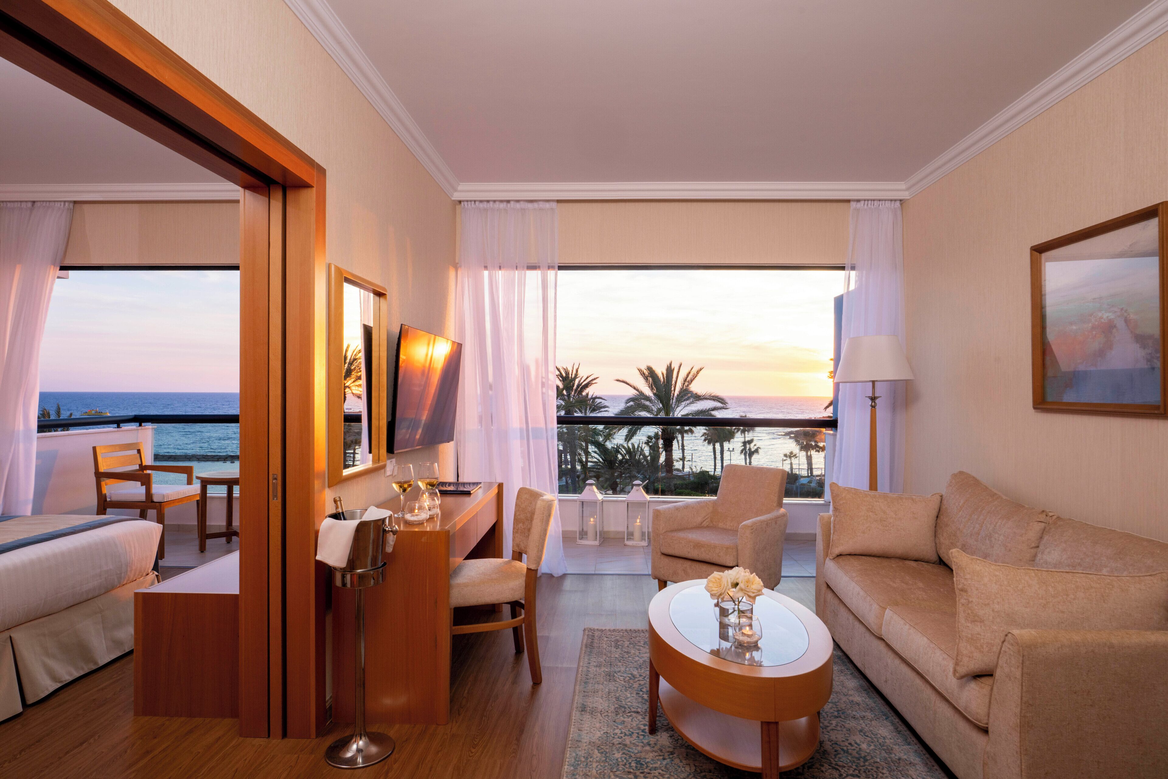 A hotel room with a balcony, a sofa, a chair, a coffee table, and a TV.