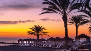 A beach with palm trees and beach huts with lounge chairs. - Constantinou Bros Asimina Suites Hotel (Geroskipou)