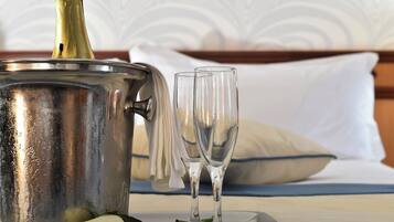 Una botella de champán en un cubo de metal, dos copas y una rosa blanca sobre una bandeja en una cama con un almohadón blanco y ropa de cama azul.