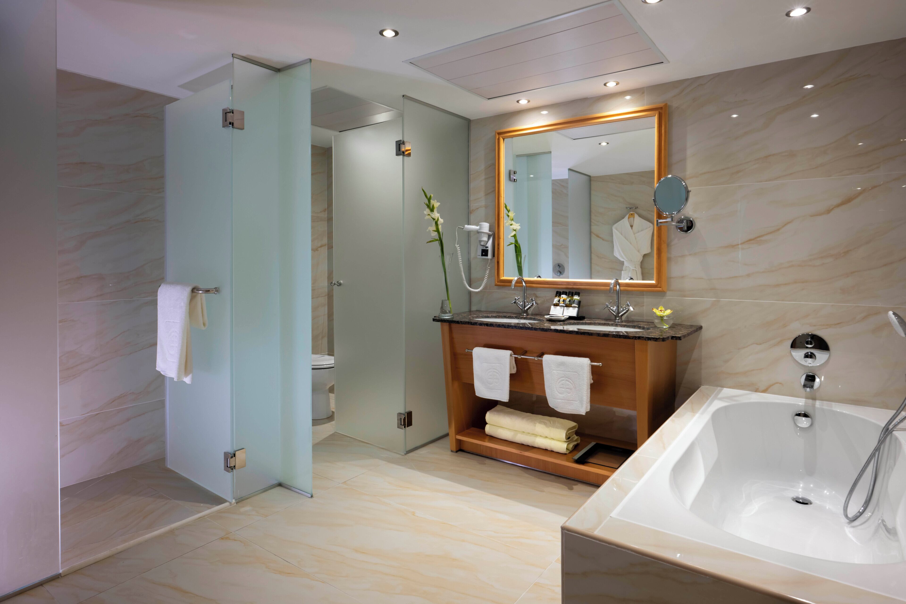 A modern bathroom with a glass shower enclosure, a wooden vanity with a mirror, and a standalone bathtub.