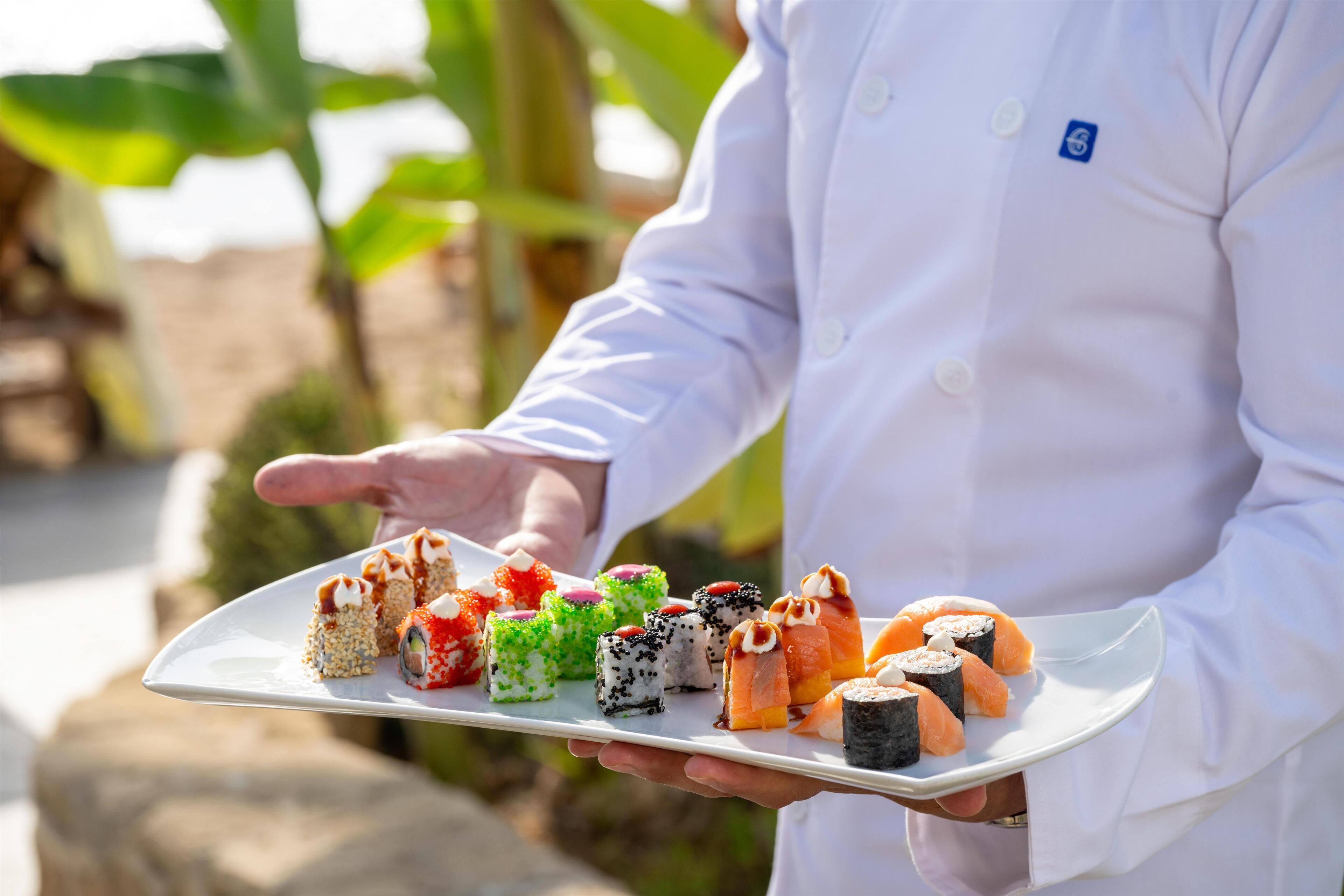 Una persona sostiene un plato blanco con diferentes piezas de sushi.