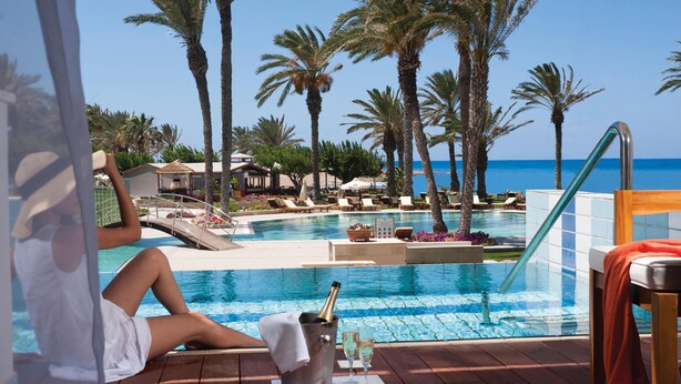 A poolside area with lounge chairs, a pool, and a view of the sea. - Constantinou Bros Asimina Suites Hotel (Geroskipou)