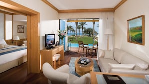 A hotel room with a bed, a desk, a sofa, a coffee table, and a view of the pool and palm trees. - Constantinou Bros Asimina Suites Hotel (Geroskipou)