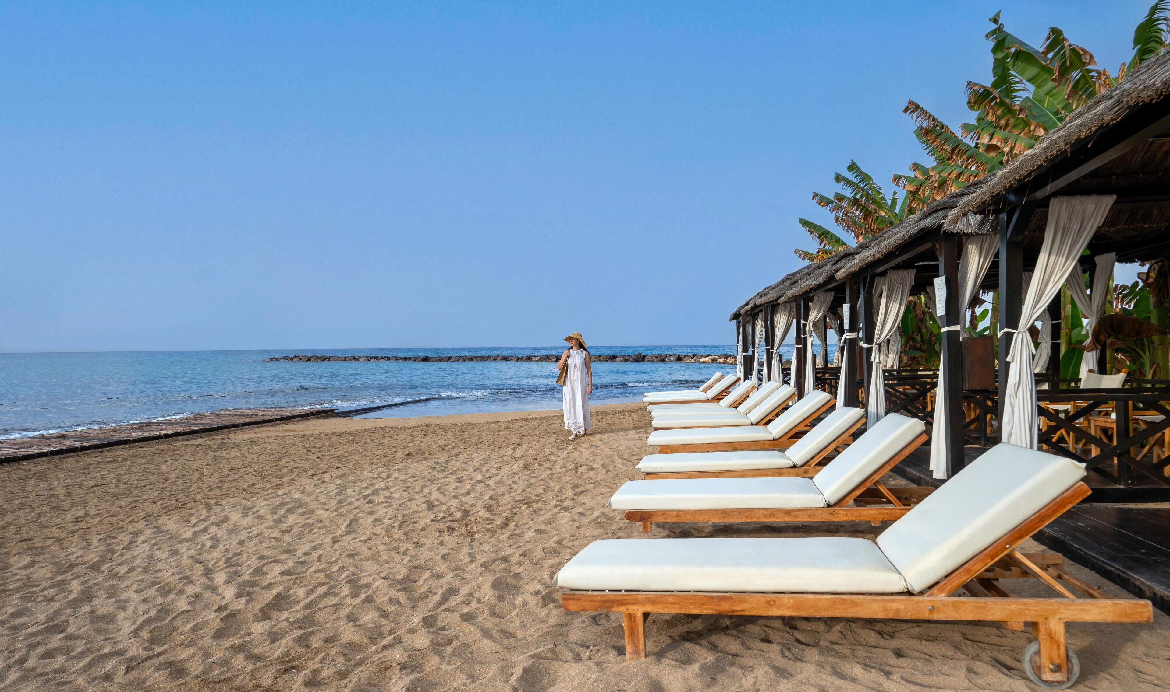A beach with lounge chairs and a person walking.