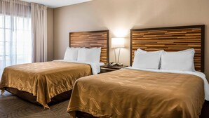Habitación de hotel con dos camas, cada una con cabecero de madera, ropa de cama blanca y una lámpara de noche.
