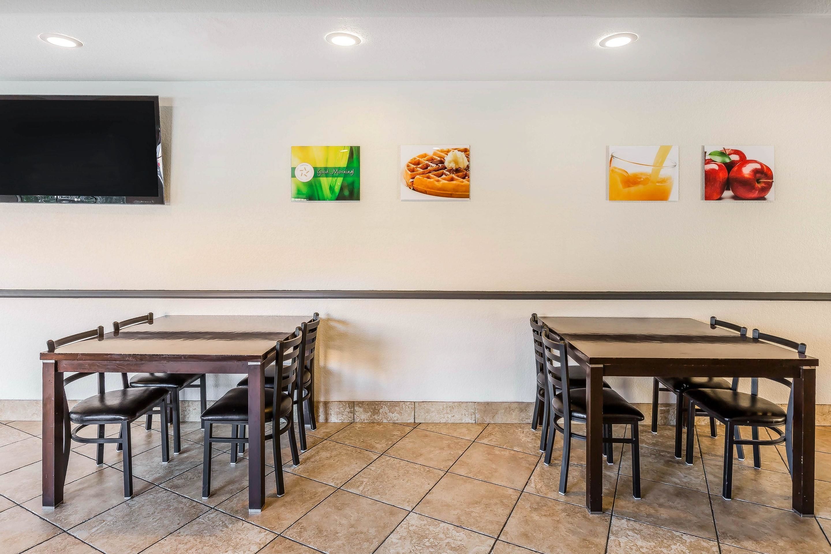 Un coin repas équipé d’un grand téléviseur à écran plat fixé au mur, d’une table en bois avec six chaises et de trois tableaux représentant différents plats.