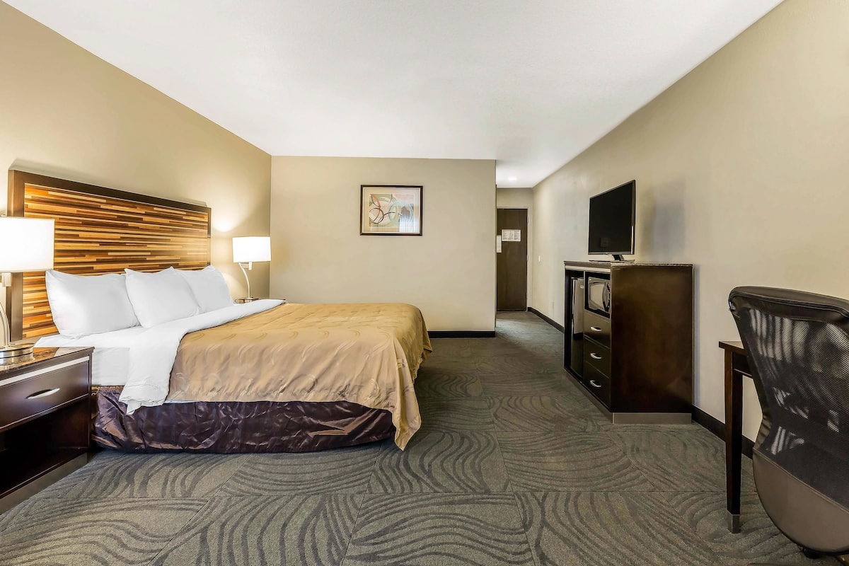 A hotel room with a bed, bedside tables, a TV, a dresser, and a chair.