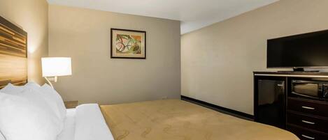 A hotel room with a bed, a television, a desk, and a wall-mounted artwork.