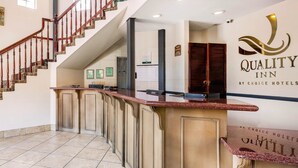 Un área de recepción con mostrador de mármol, una escalera y un cartel de Quality Inn by Choice Hotels.