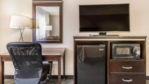 Una habitación de hotel con escritorio, una silla, televisor, refrigerador y microondas.