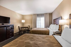 A hotel room with two beds, a desk, a TV, and a window with curtains.