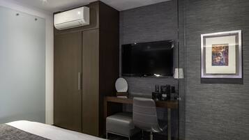 Quarto de hotel moderno com cama, escrivaninha com cadeira, televisão de tela plana, ar-condicionado e quadro na parede.