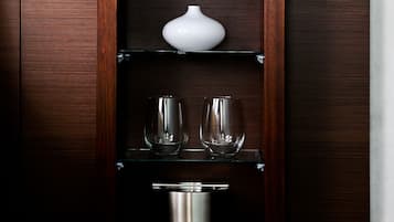 A wooden cabinet with a white vase and two glasses on the top shelf, and a metallic container on the bottom shelf.