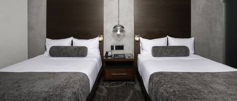 Ein Hotelzimmer mit zwei Betten, einem Nachttisch in der Mitte mit Telefon und Lampe, und einem modernen Design mit Beton- und Holzelementen.