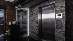 Een lift met een digitaal bedieningspaneel, een deur met een glazen ruit en een wand met een reliëf van steen.