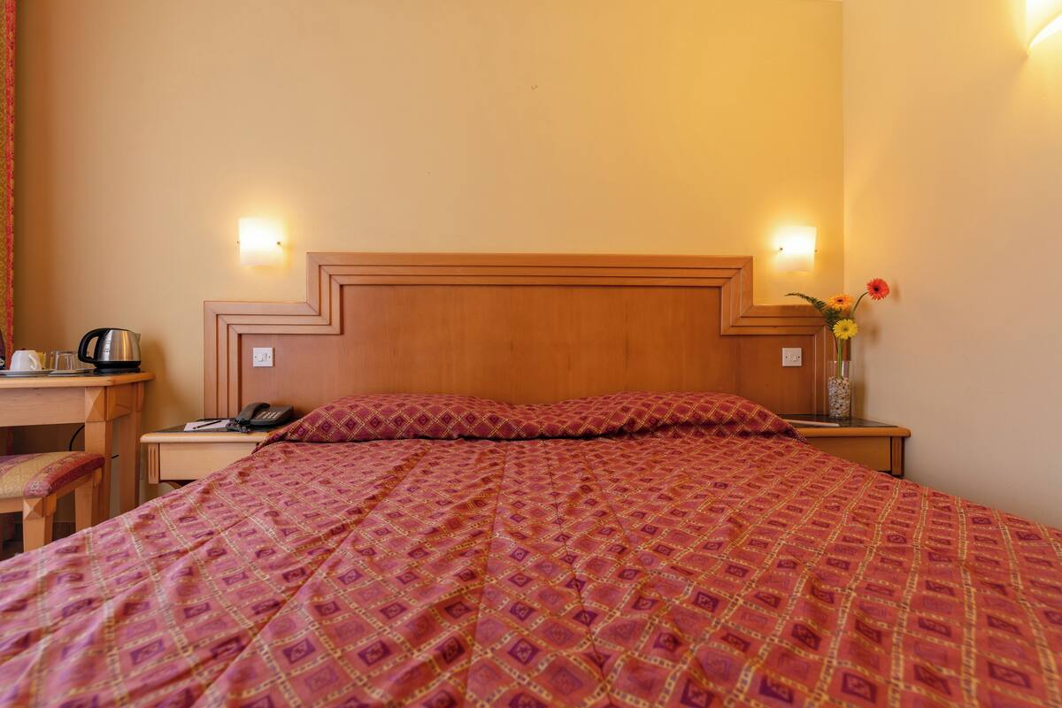 Una habitación de hotel con una cama grande, cabecero de madera, mesitas de noche, un escritorio y una silla.