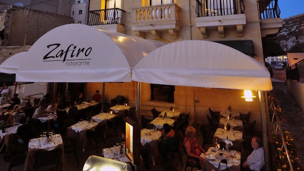 Um edifício com várias varandas e um restaurante chamado "Zafiro" com área externa.