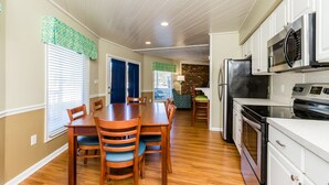A kitchen with white cabinets, a microwave, an oven, and a dining area with a wooden table and chairs.