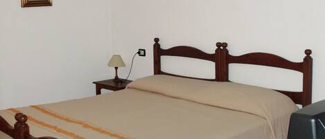 A single bed with a wooden frame, a bedside table with a lamp, and a television on a stand.