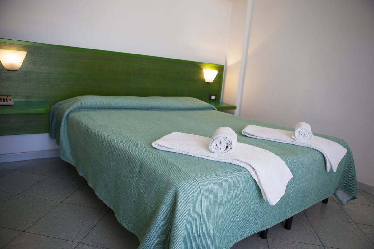 A hotel room with two beds, green headboards, and white towels.