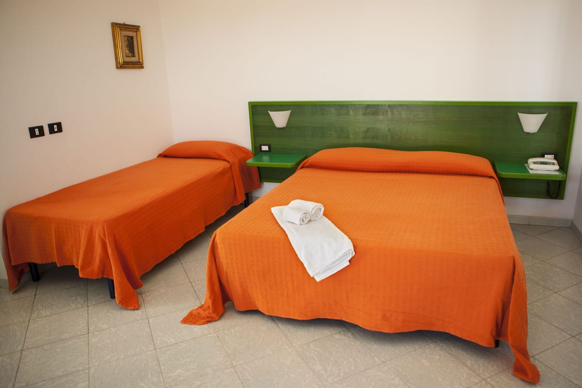 Two single beds with orange bedding and green headboards in a room with a tiled floor.