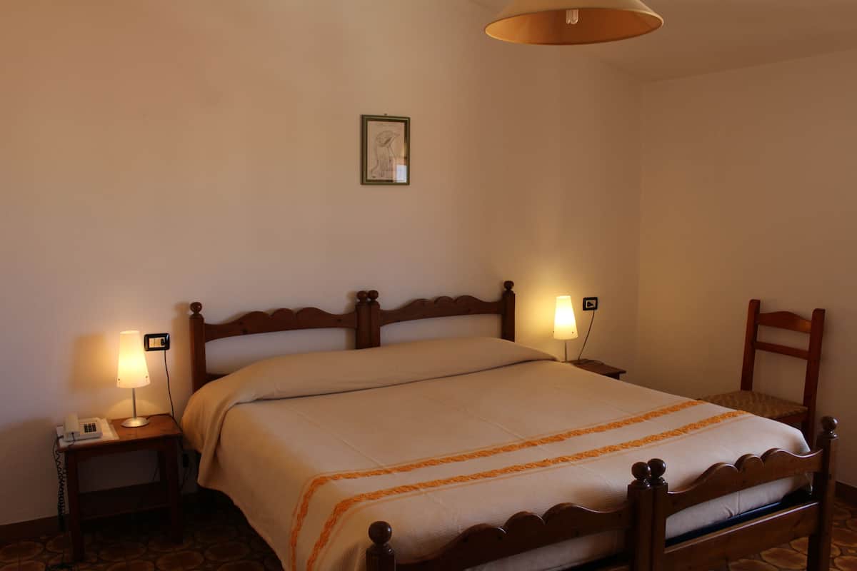 A neatly made bed with a wooden headboard, two bedside lamps, and a small bedside table with a phone.