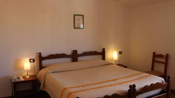 Una cama bien hecha con cabecera de madera, dos lámparas de noche y una mesita de noche con un teléfono.