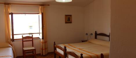 A bedroom with two single beds, a wooden chair, a window with curtains, a ceiling light, and a framed picture on the wall.