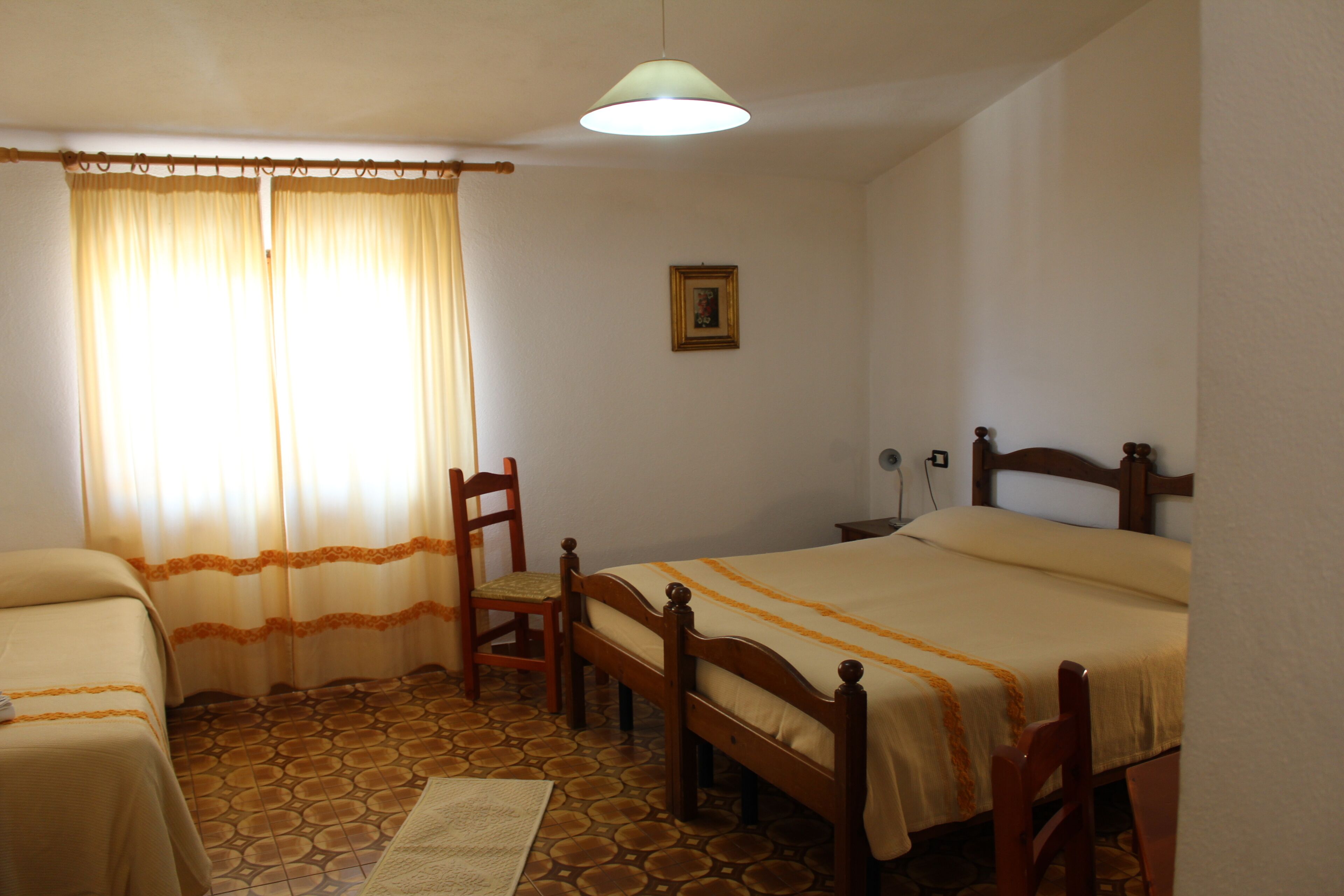 Una habitación con dos camas, una silla, una lámpara y un cuadro en la pared.