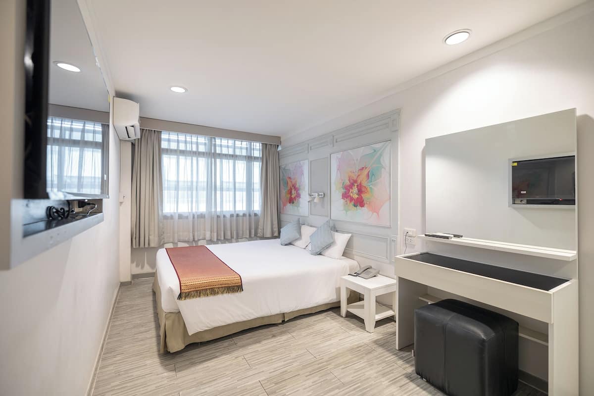 A modern hotel room with a large bed, a desk, a chair, a TV, and a window with curtains.