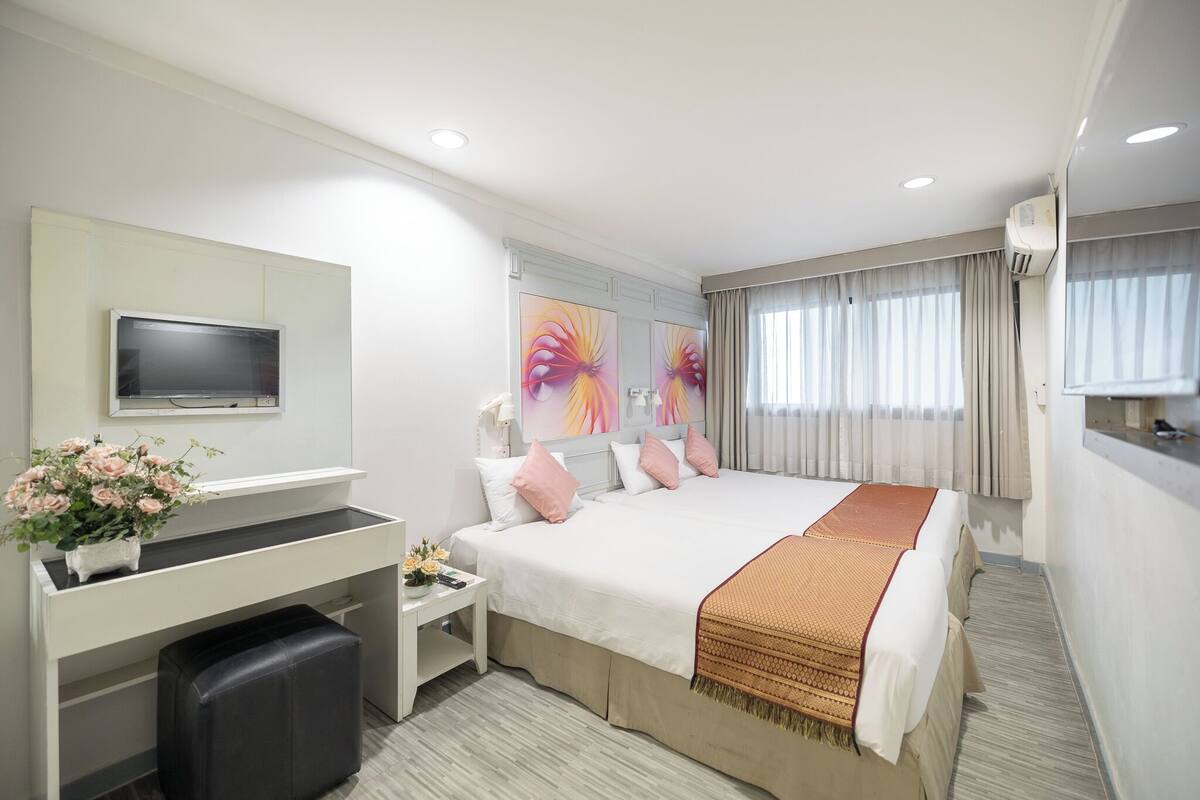 A modern hotel room with a large bed, a desk with a computer, a TV, and artwork on the wall.