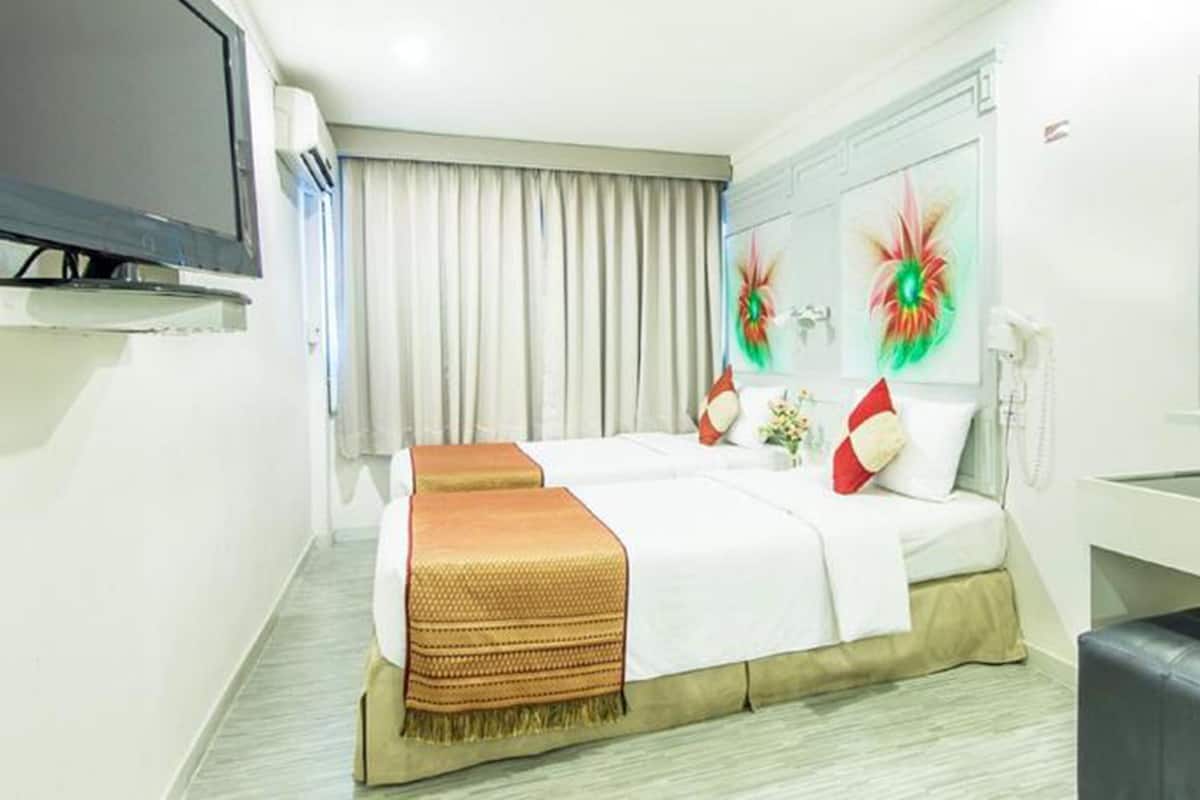 A hotel room with a bed, a TV, a trash bin, and a wall with two decorative items.