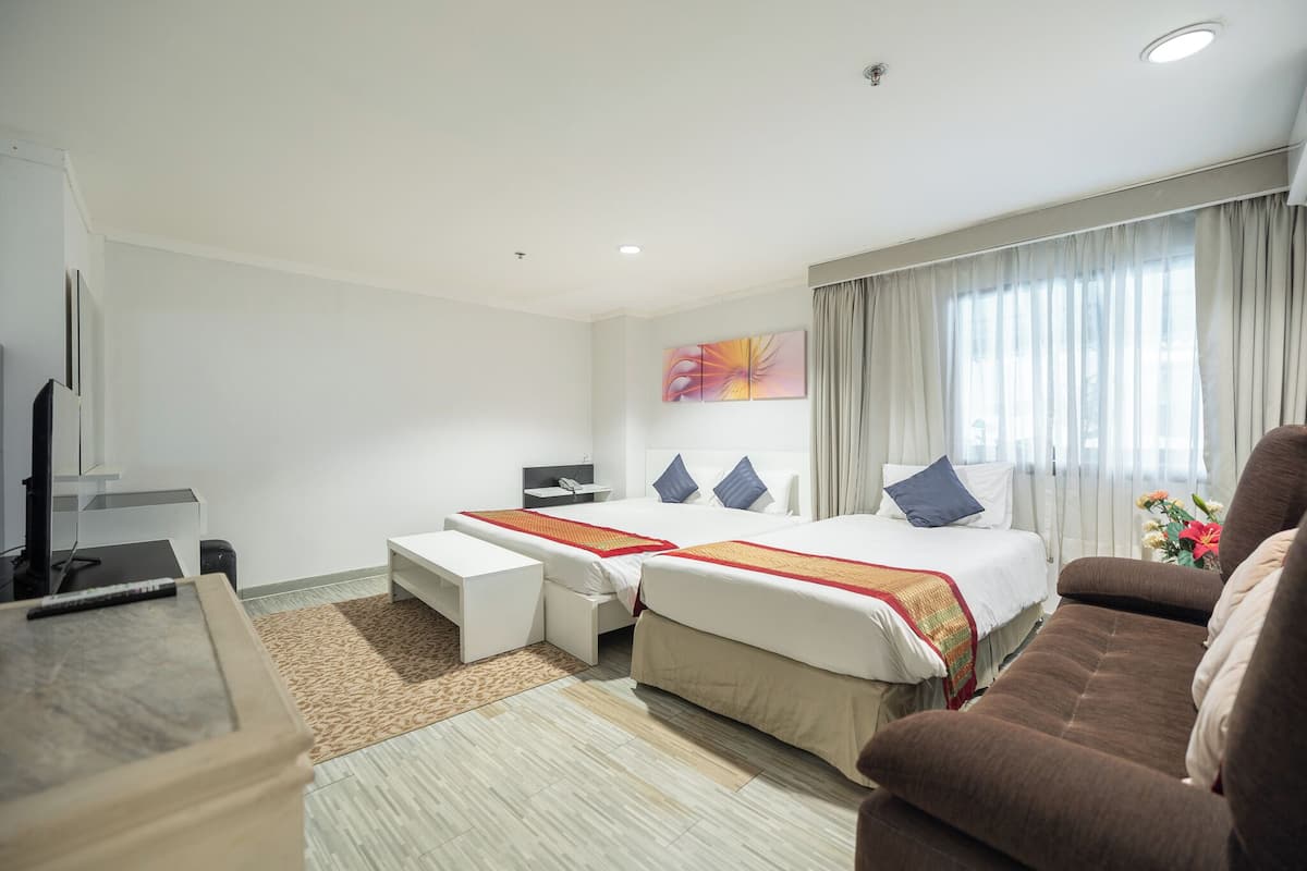 A hotel room with two beds, a sofa, a desk, and a TV.