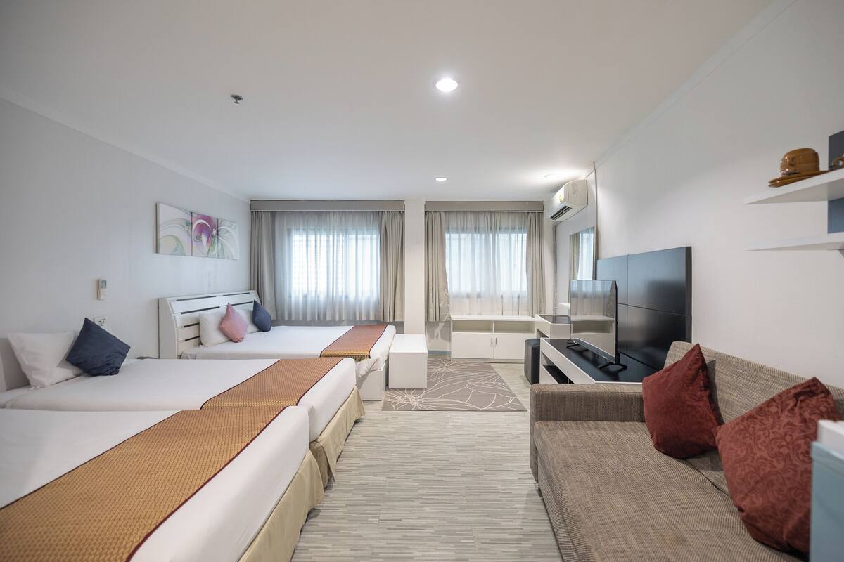 A hotel room with two beds, a sofa, a TV, and a desk.