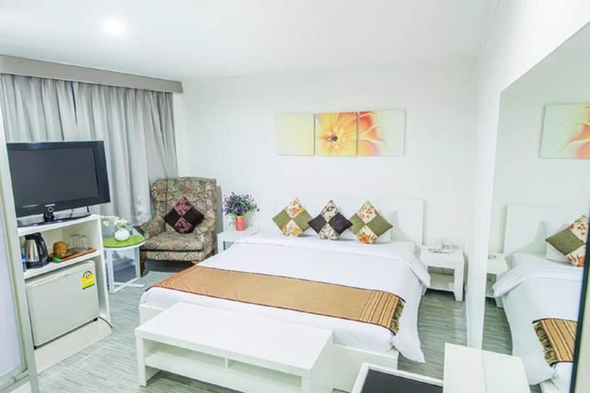 A hotel room with a bed, a TV, a chair, a small table, and a mirror.