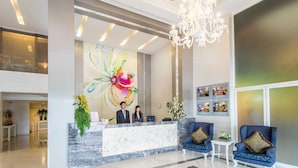 A hotel reception area with a marble counter, two receptionists, a chandelier, and a large floral mural. - Pratunam City Inn (Bangkok)