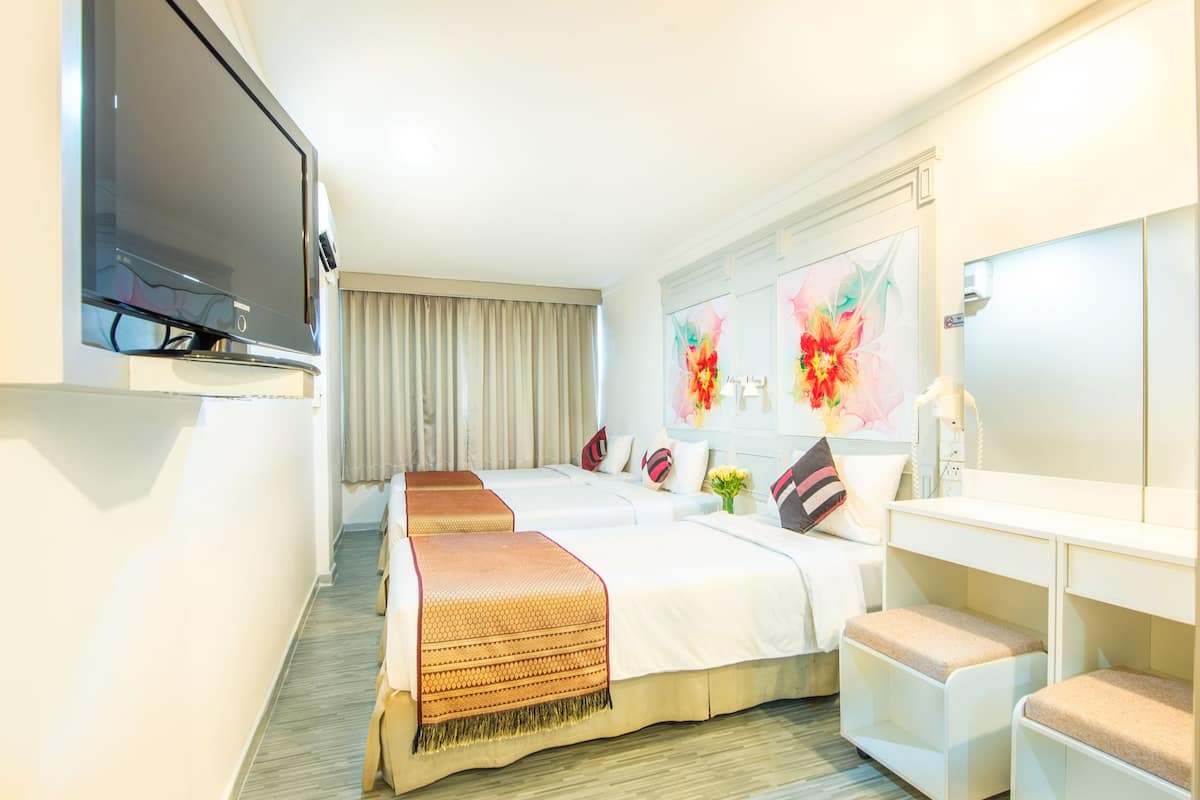 A hotel room with two beds, a TV, a desk, and artwork on the wall.