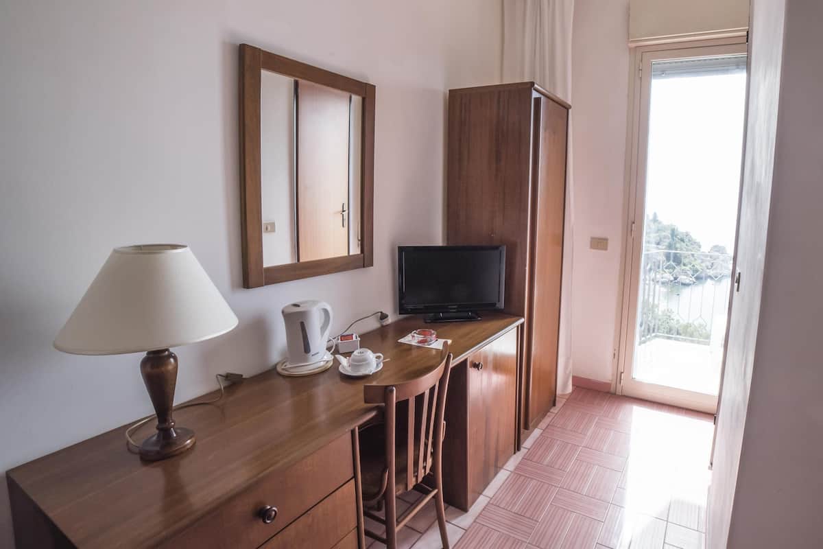 A hotel room with a wooden desk, a television, a lamp, and a view of the outside balcony.